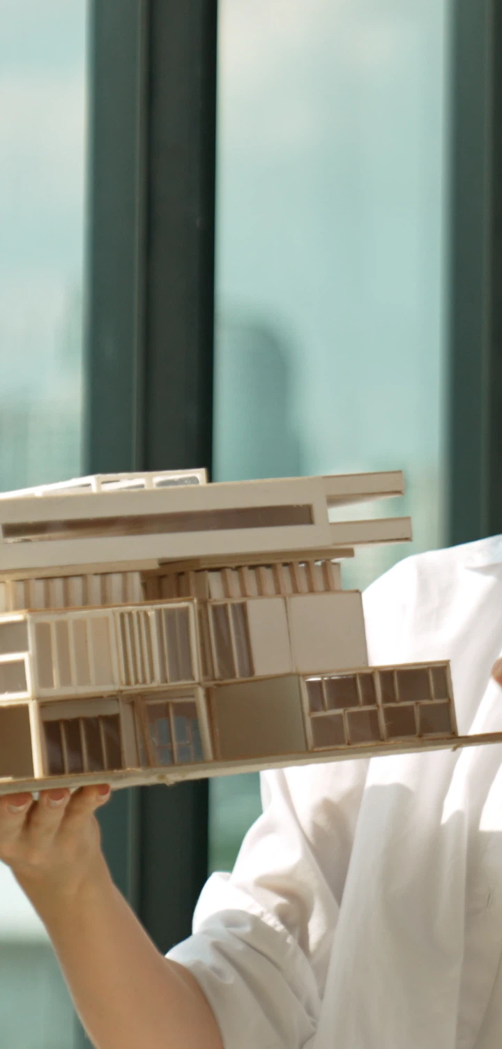 Maqueta branca de um edifício segurada junto a uma janela